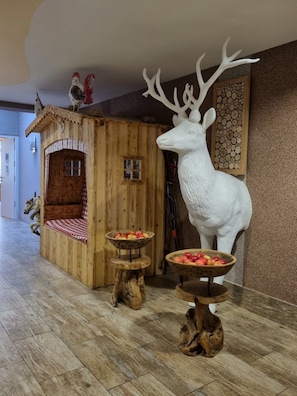 Un interior rústico con una casita de juegos de madera, una gran escultura de ciervo y dos mesas de madera con fruteros.