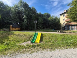 A playground with a green and yellow slide, surrounded by grass and trees.