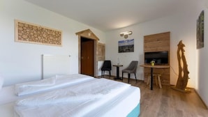 Hotellihuone, jossa on sänky, työpöytä, tuoli, televisio ja puinen seinäpaneeli.