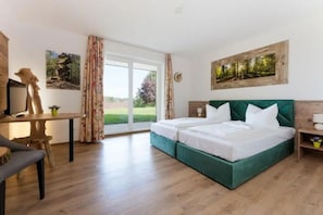 Un dormitorio con cama, escritorio y silla. Hay dos ventanas con cortinas.
