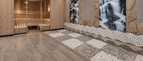 A sauna room with wooden benches, a stone wall with a waterfall mural, and a starry ceiling.