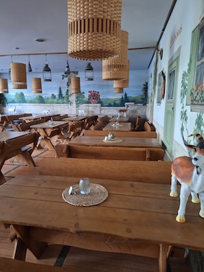 A restaurant with wooden tables and benches, wicker hanging lamps, and a mural on the wall.