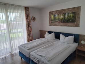 Una cama doble con sábanas blancas, cabecera de madera y mesita de noche con lámpara.