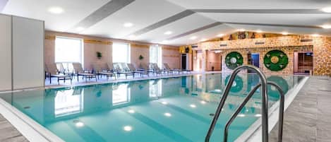 A swimming pool with a clear blue water surface, surrounded by lounge chairs and a stone wall with decorative elements.