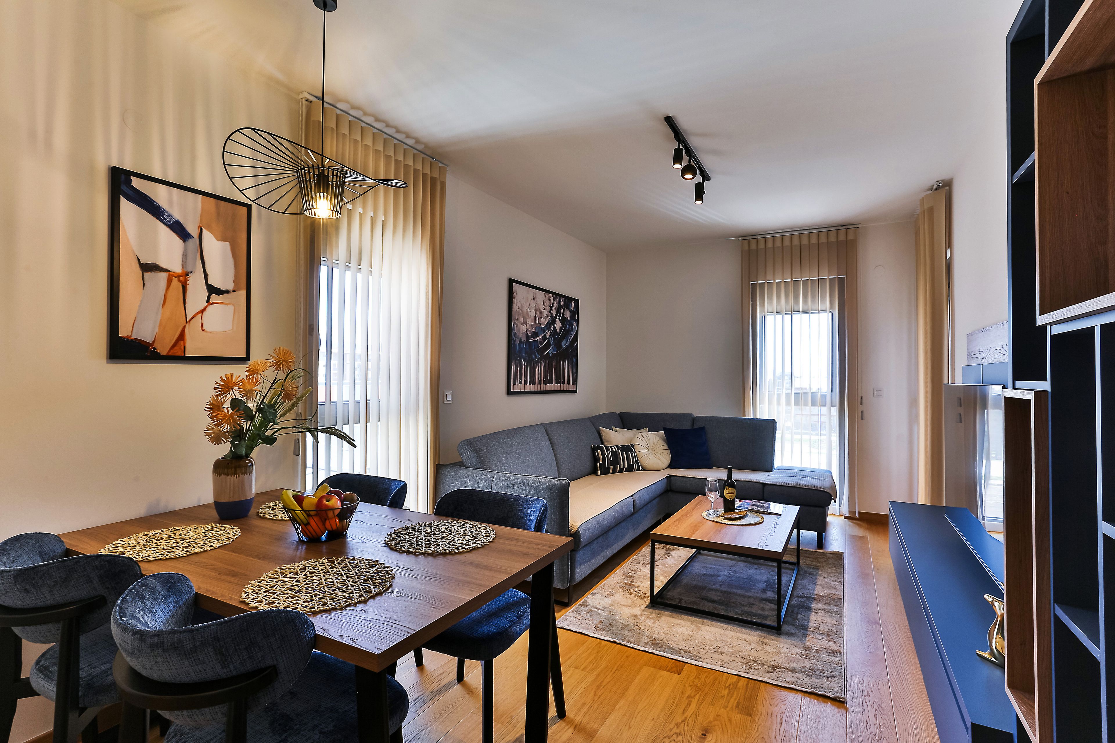 A modern living room with a wooden dining table, blue sofas, and a coffee table.