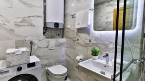 Een moderne badkamer met een ingebouwde wasmachine, toilet, wastafel en een douchecabine van glas.