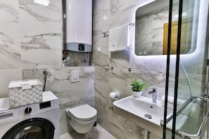 Un baño moderno con lavadora integrada, inodoro, lavamanos y mampara de vidrio.