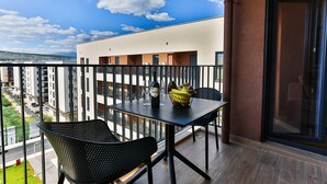 Een balkon met een tafel en stoelen, een fles wijn en een schaal fruit.