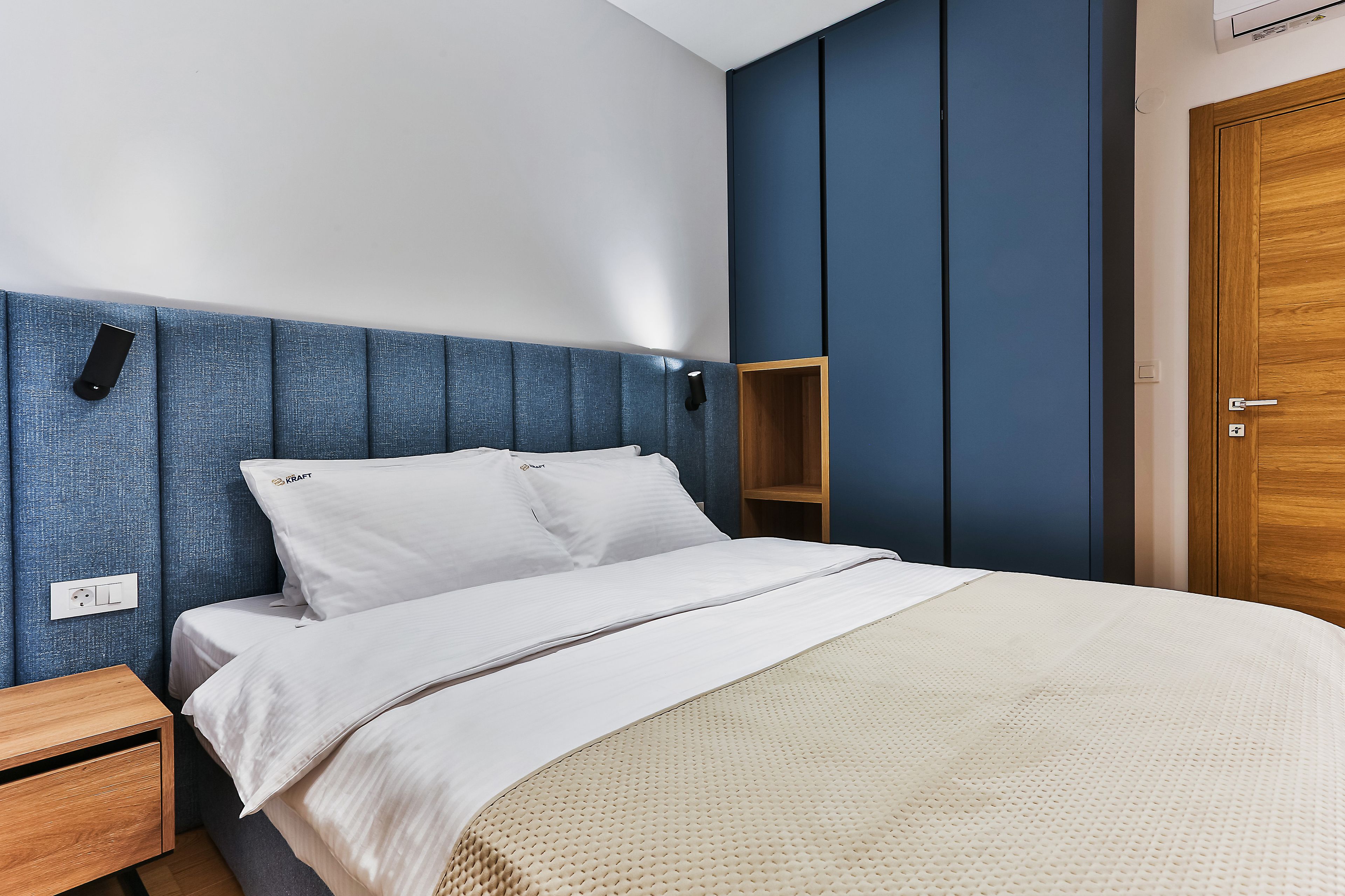Un dormitorio con una cama, una mesita de noche, un armario de madera y una estantería de pared.