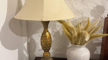 Une lampe avec un abat-jour beige et un pied décoratif, posée sur une table en bois à côté d’un vase blanc contenant des plantes séchées.