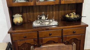A wooden cabinet with glass-fronted compartments containing glassware and a tray with silverware.