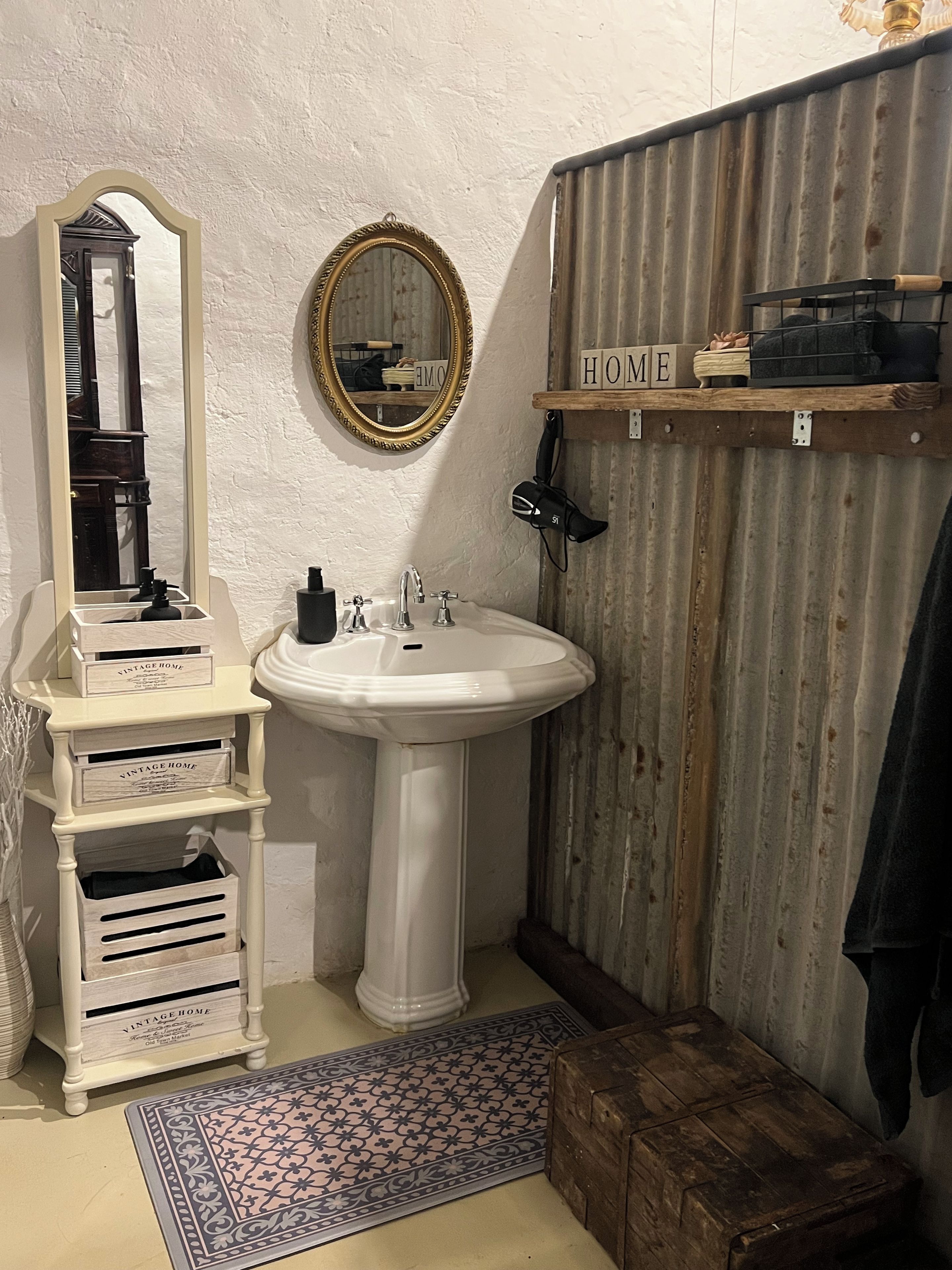 Ein Badezimmer mit einem Standwaschbecken, einem Spiegel, einem Waschtisch mit Stauraum, einer Duschkabine und einer hölzernen Sitzbank.