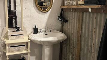 Ein Badezimmer mit einem Standwaschbecken, einem Spiegel, einem Waschtisch mit Stauraum, einer Duschkabine und einer hölzernen Sitzbank.
