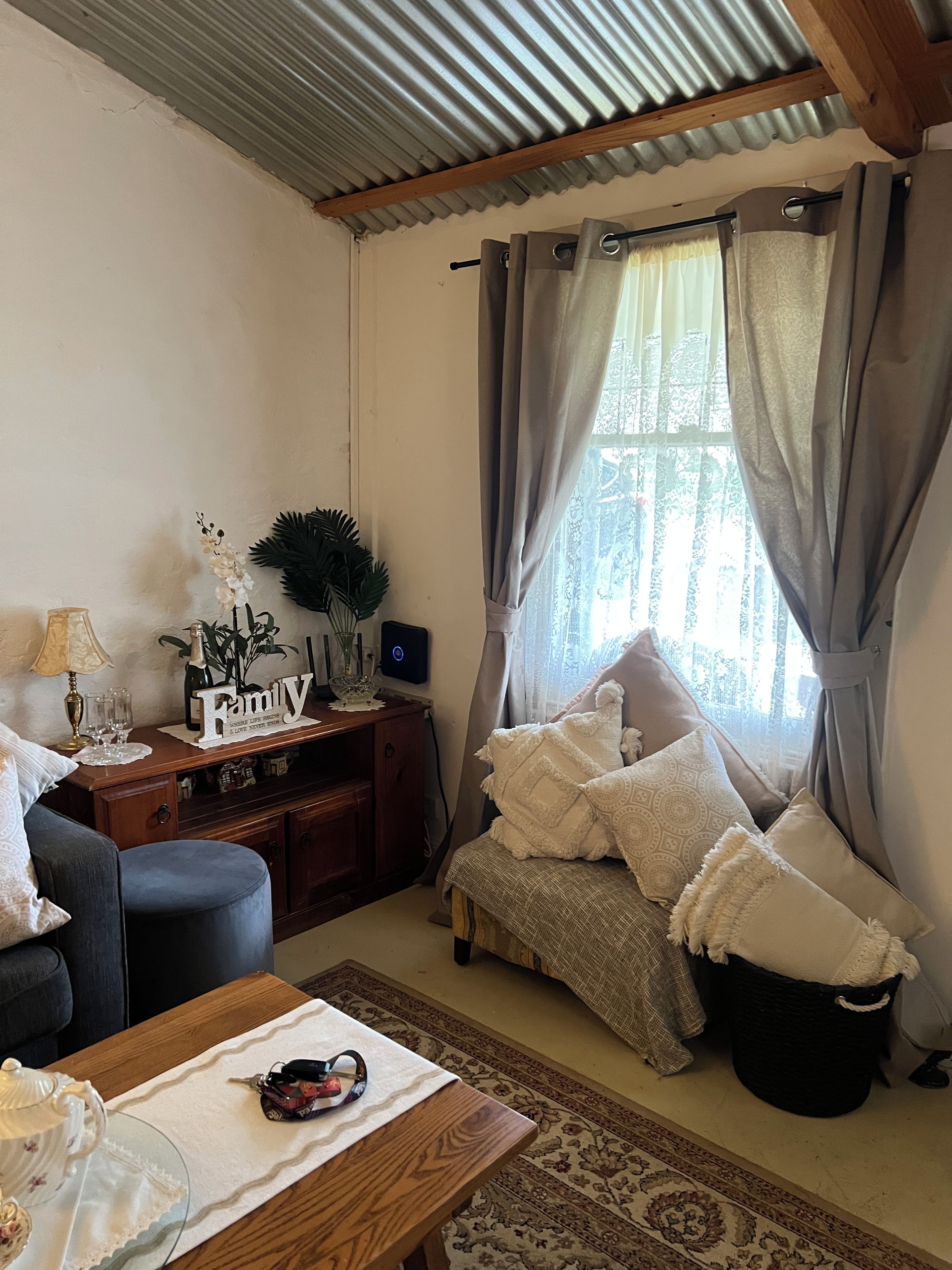 Ein gemütliches Wohnzimmer mit einer Couch, einem Holztisch, einer Zierdevasse und einem Fenster mit Vorhängen.