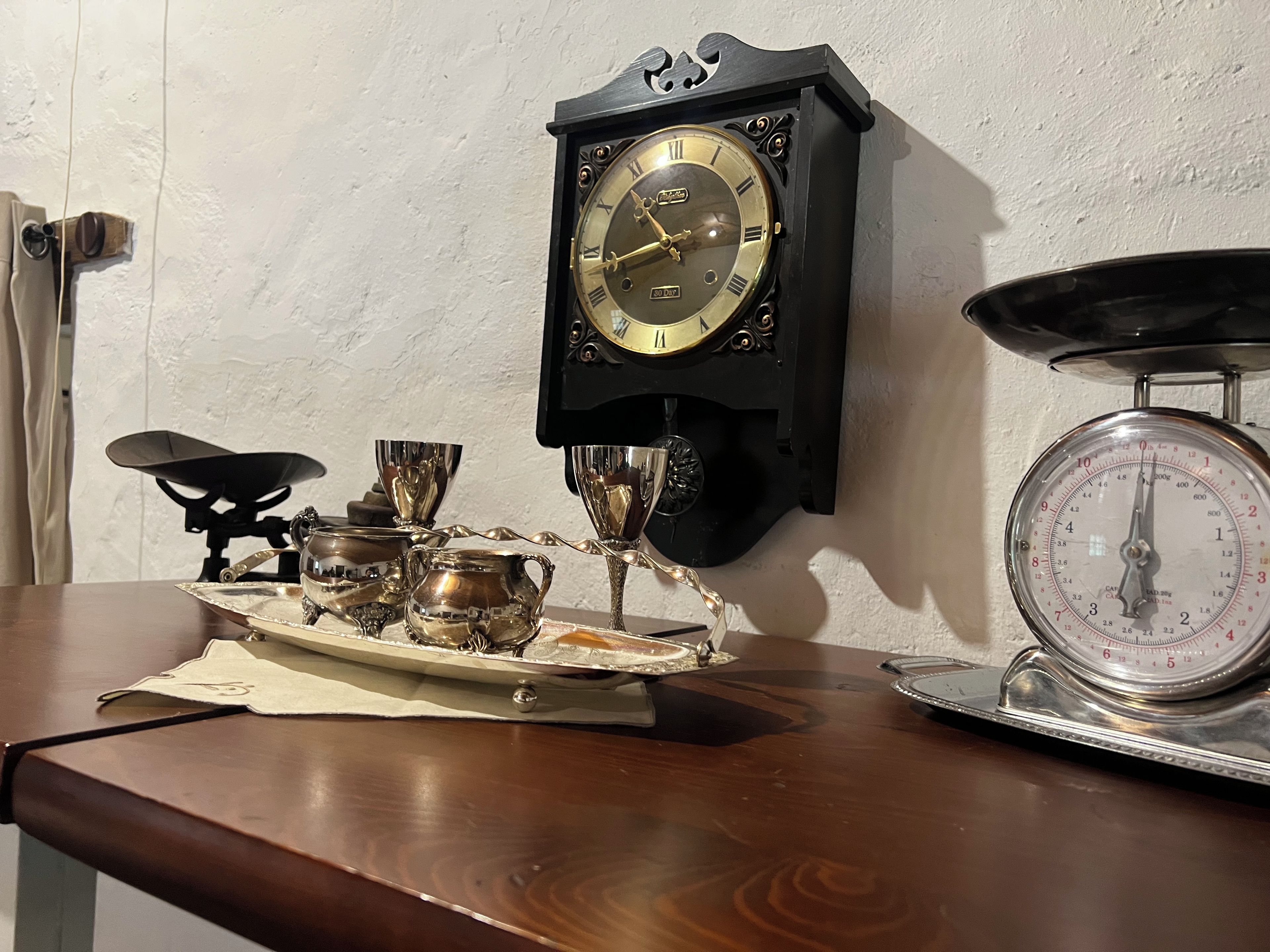 Un reloj de pared antiguo con números romanos, una balanza y una bandeja con cubiertos y una jofaina.