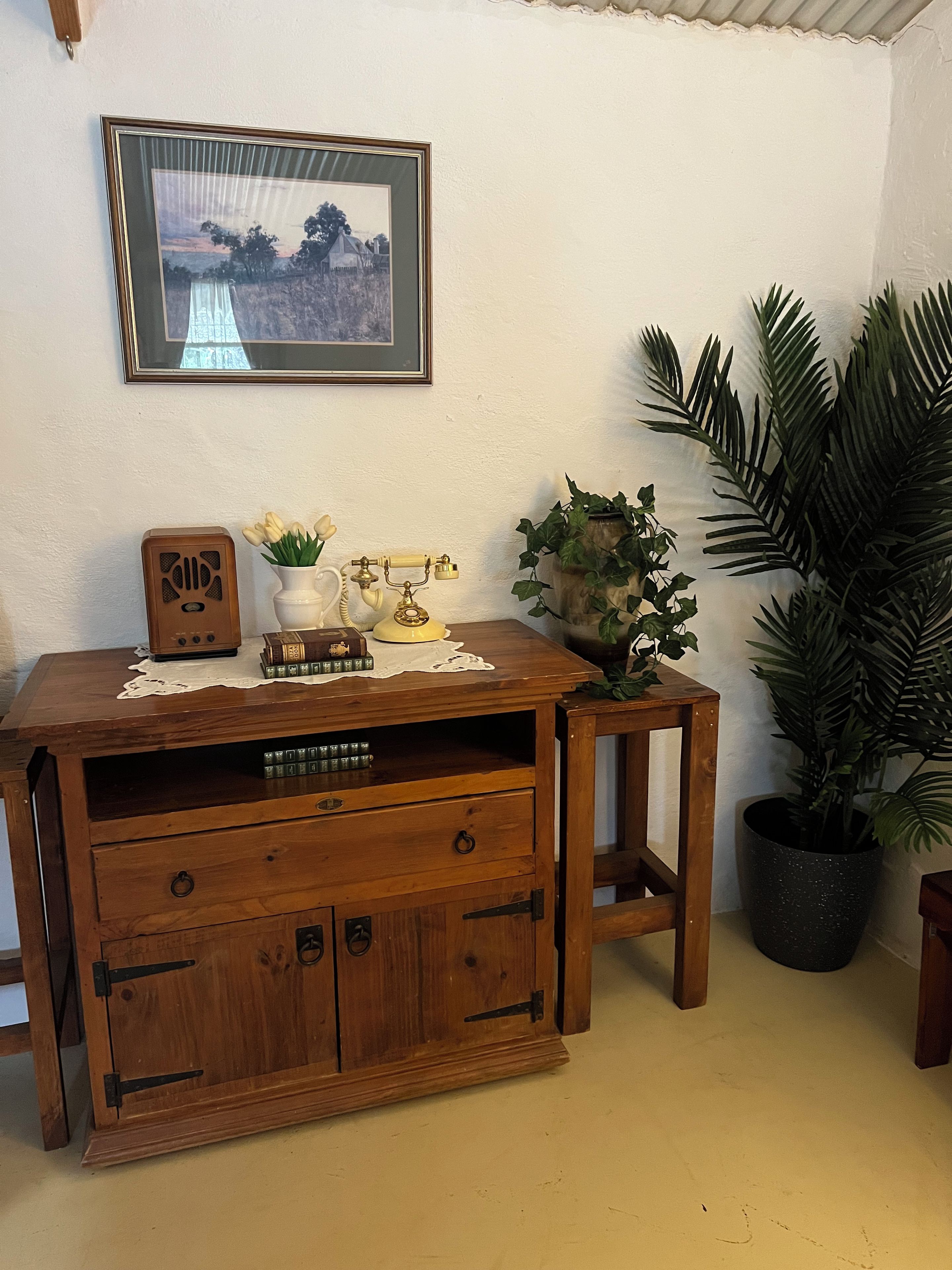 A wooden desk with drawers, a vintage telephone, a framed picture, and a potted plant.
