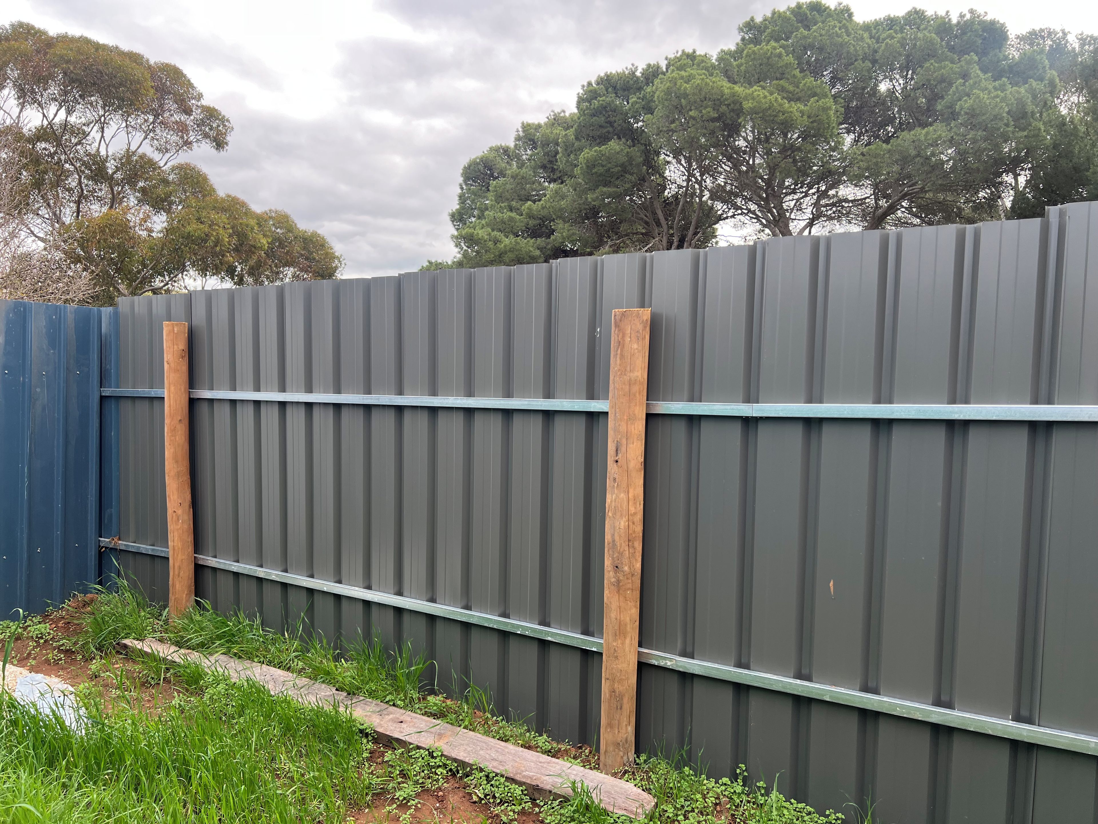 A corrugated metal fence with wooden posts and a blue fence on one side.