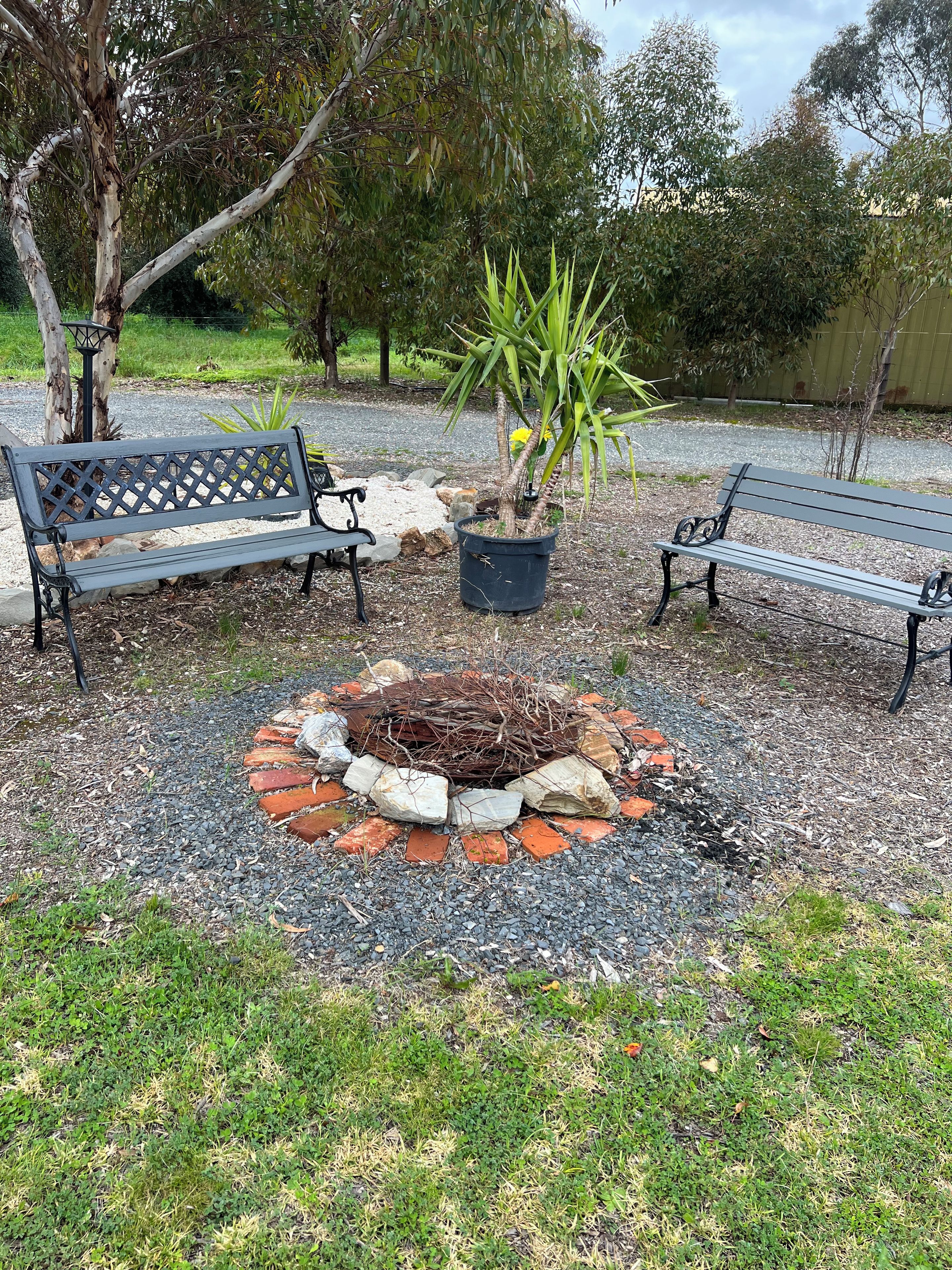 A park with two benches, a small fire pit, and a potted plant.