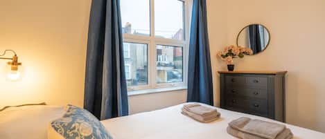 Een hotelkamer met een bed, een dressoir, een spiegel en een raam met gordijnen.