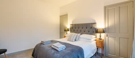 A bedroom with a large bed, a bedside table with a lamp, a door, and a carpeted floor.