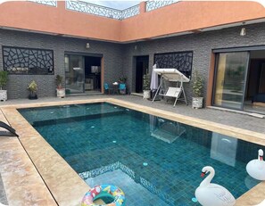 Ein Swimmingpool mit Schwanein und Enten-Schwimmspielzeug, umgeben von Blumentöpfen und einer überdachten Sitzgelegenheit.
