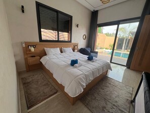 Ein Schlafzimmer mit einem großen Bett, einem Nachttisch, einer Fensterbank und Blick ins Freie.