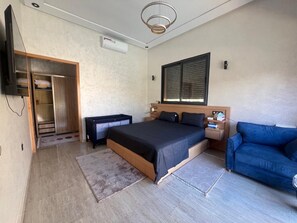 Ein Schlafzimmer mit einem Bett, einem blauen Sofa, einem Fernseher und einem Fenster mit Jalousien.