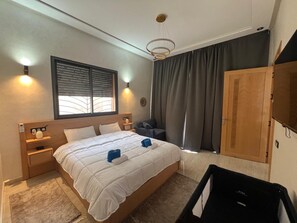 Ein Hotelzimmer mit Bett, Nachttischen, einem Kleiderschrank, einem Fenster mit Jalousien und einer Deckenleuchte.