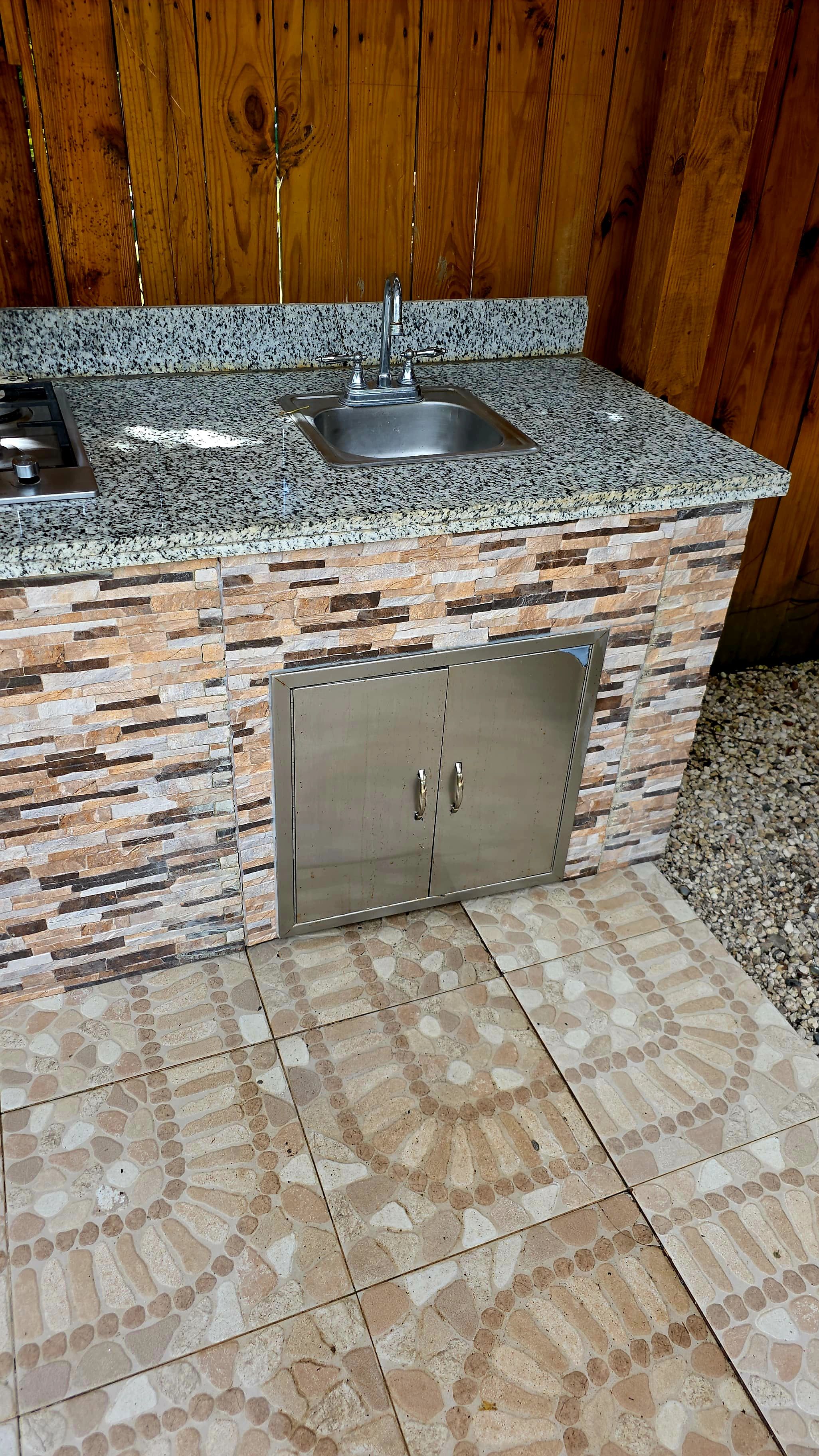 Cozinha com bancada de granito, pia de aço inoxidável e painel de pedra.