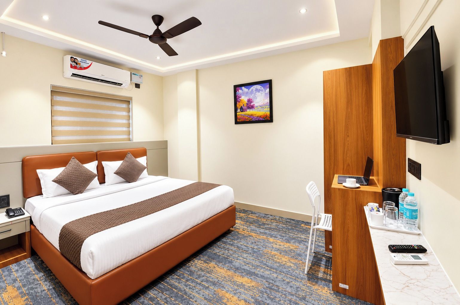 Habitación de hotel con cama, escritorio con computadora, televisor, equipo de aire acondicionado y un cuadro en la pared.