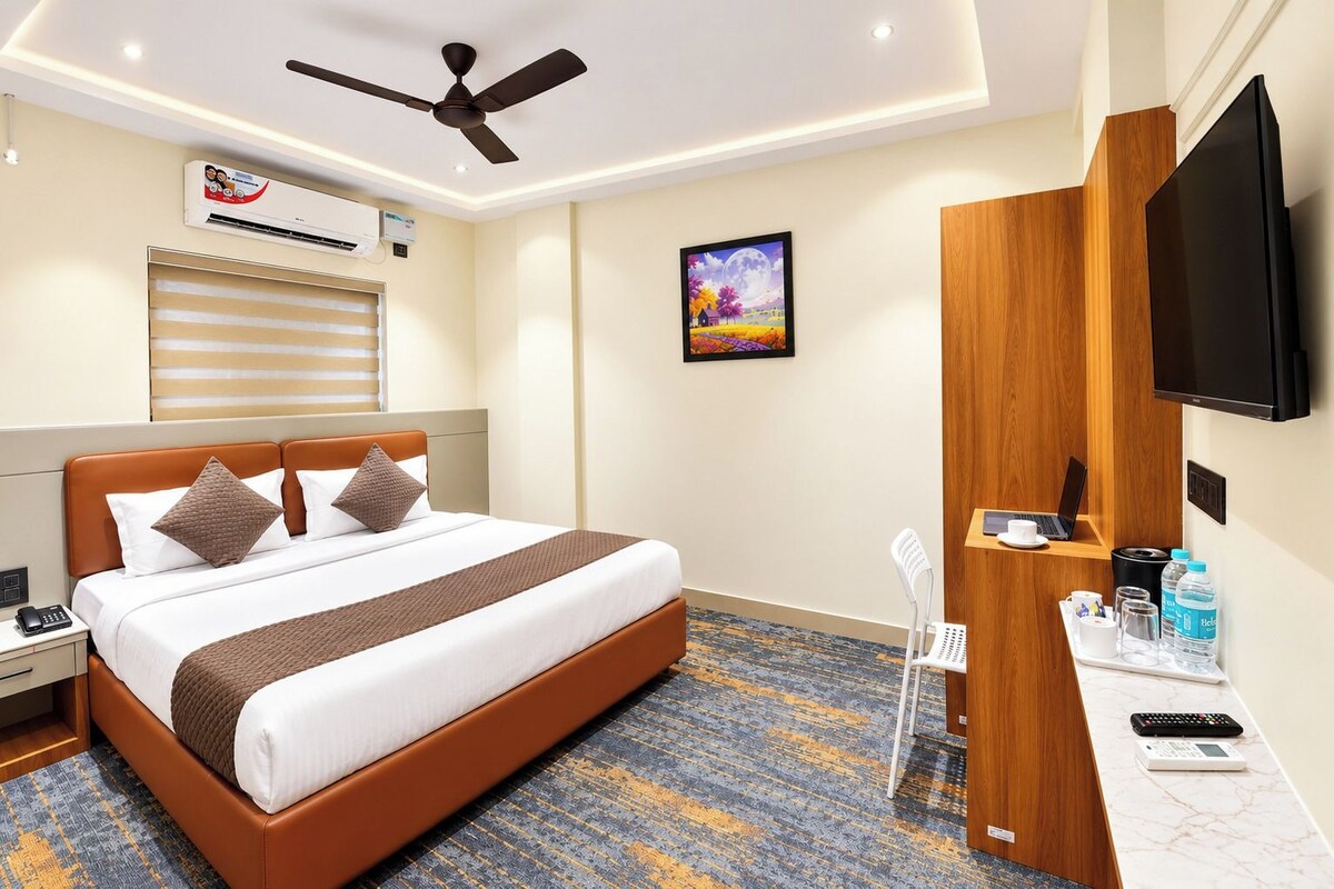 Een hotelkamer met een bed, een bureau met een computer, een televisie, een airconditioner en een schilderij aan de muur.