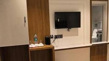 Habitació d'hotel amb un llit, un televisor fixat a la paret, un armari de fusta i una taula petita amb una ampolla i una tassa.