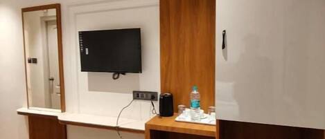 Habitación de hotel con una cama, un escritorio con televisor de pantalla plana, un espejo y un cesto de basura pequeño.