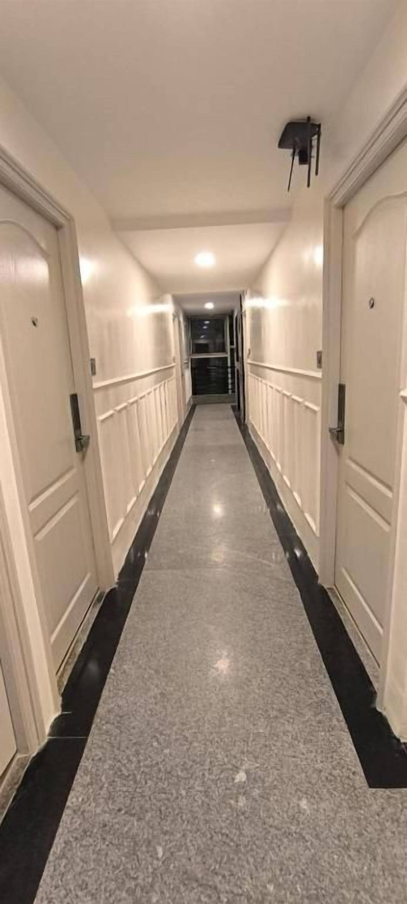 Pasillo de hotel con puertas a ambos lados, piso pulido y lámpara en el techo.