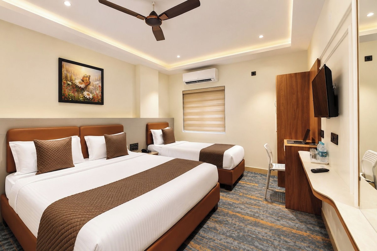 Een hotelkamer met twee bedden, een plafondventilator, een airconditioning en een bureau met een laptop en een televisie.