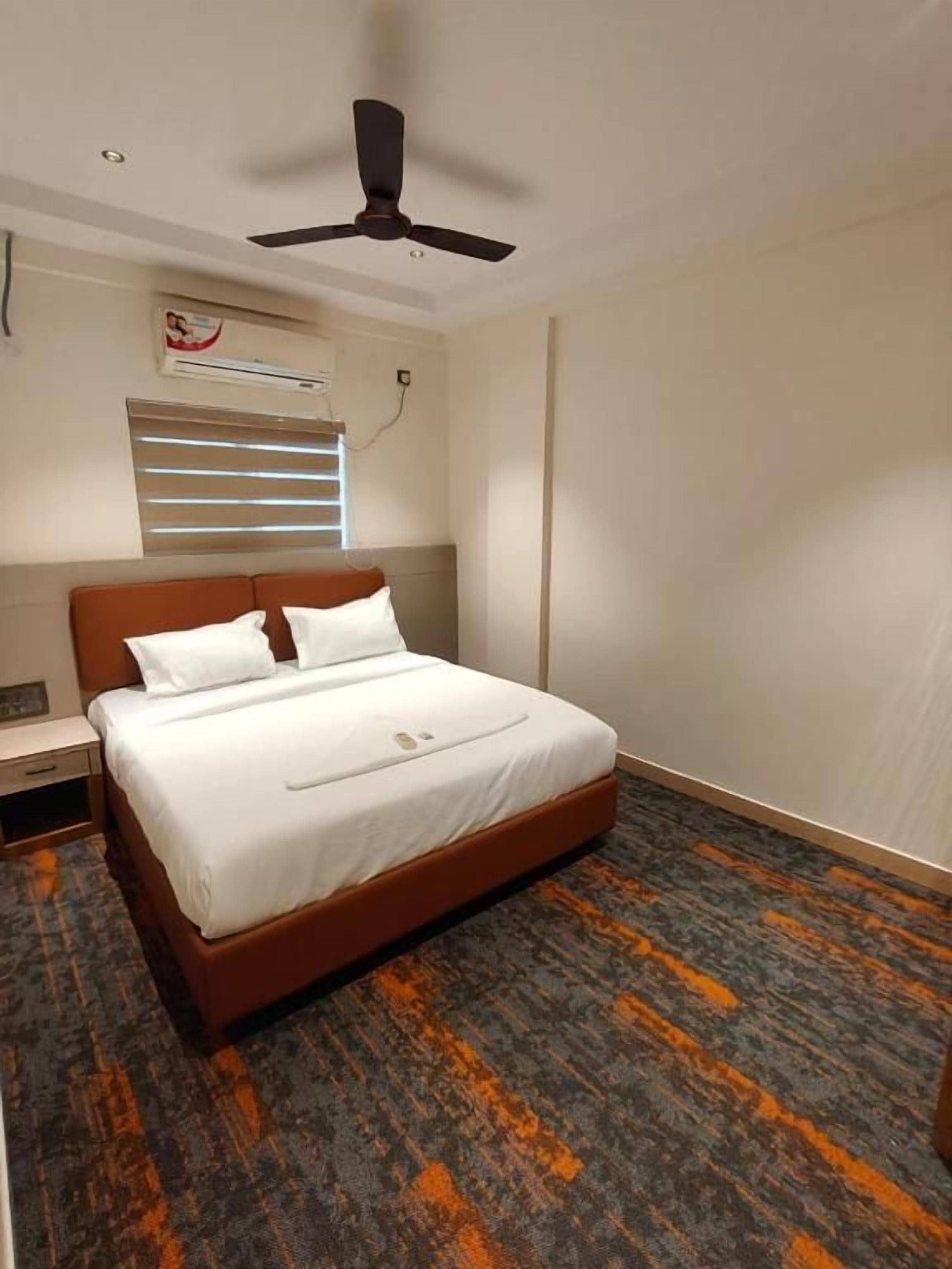 Habitación de hotel con una cama individual, ventilador de techo, aire acondicionado y ventana con persianas.