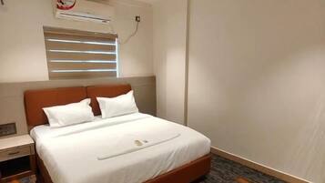 Habitación de hotel con una cama individual, ventilador de techo, aire acondicionado y ventana con persianas.