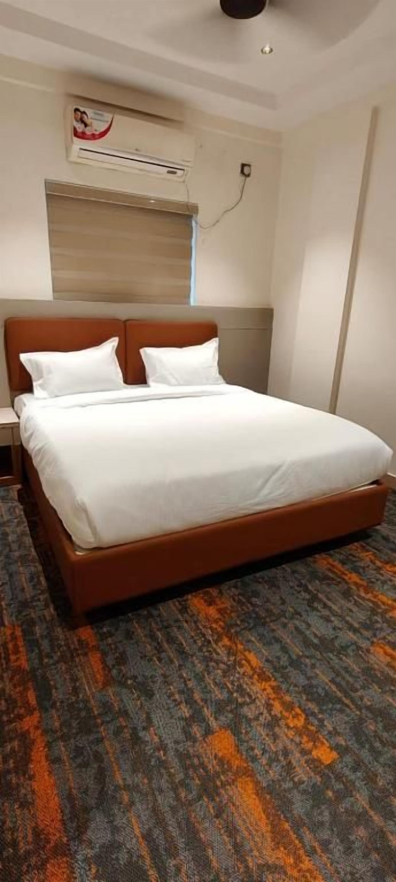 Quarto de hotel com uma cama grande, cabeceira, aparelho de ar condicionado e piso coberto por carpete.