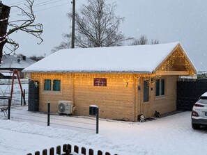 A wooden cabin with a snow-covered roof, a sign indicating a restaurant, and a fenced yard.
