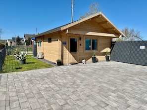A wooden building with a sloped roof, a paved driveway, and a fenced area with potted plants.
