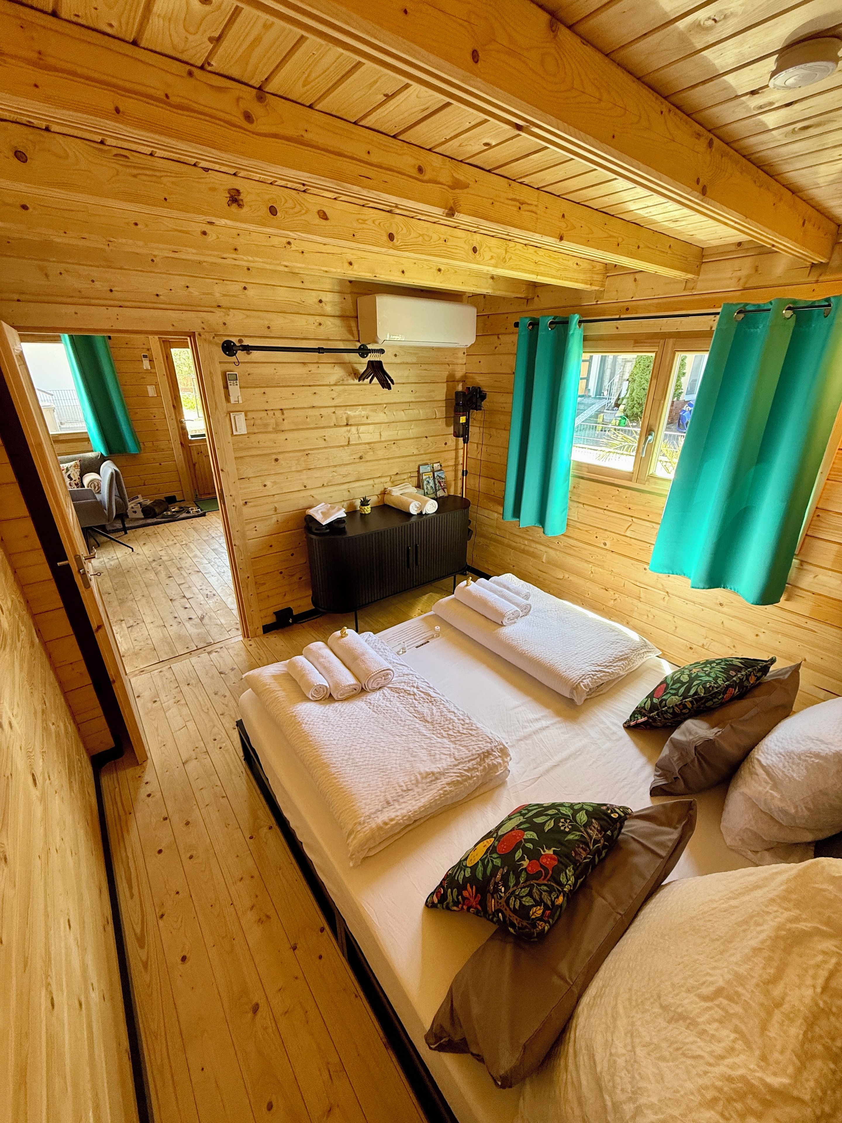 Une chambre dans un chalet en bois, avec un lit, des serviettes, des oreillers, un radiateur et une fenêtre avec des rideaux.