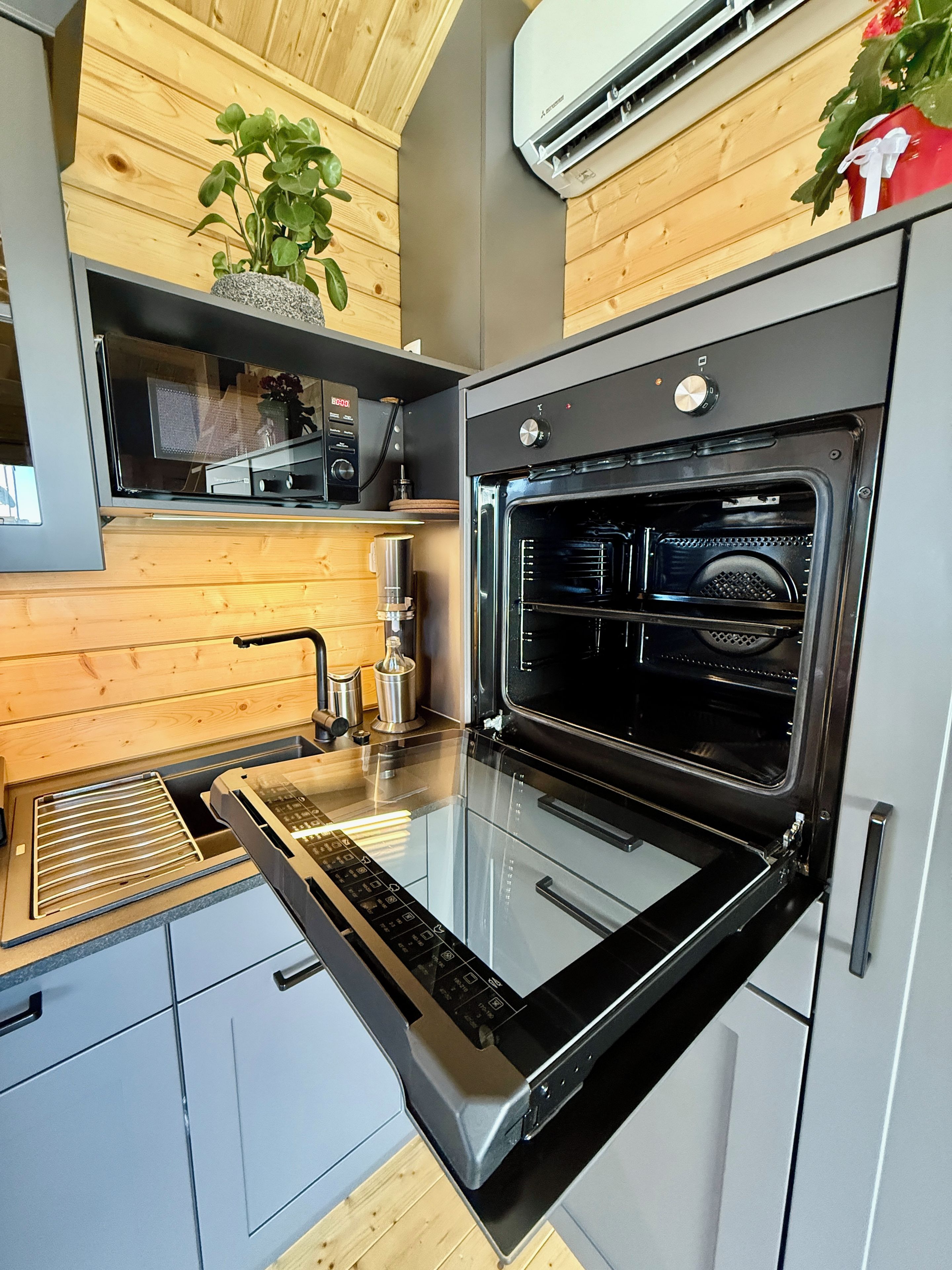 Eine moderne Küche mit eingebautem Ofen, einem Edelstahl-Dunstabzug und einer Holzrückwand.