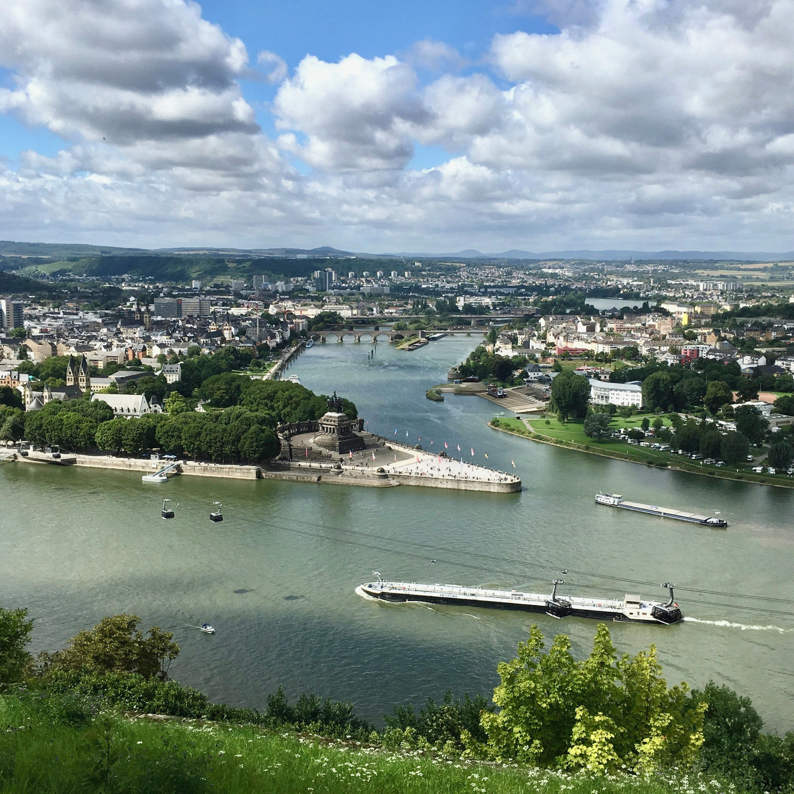 Ein Fluss mit Booten, einer Brücke und einer Stadtlandschaft mit Gebäuden und Grünflächen.