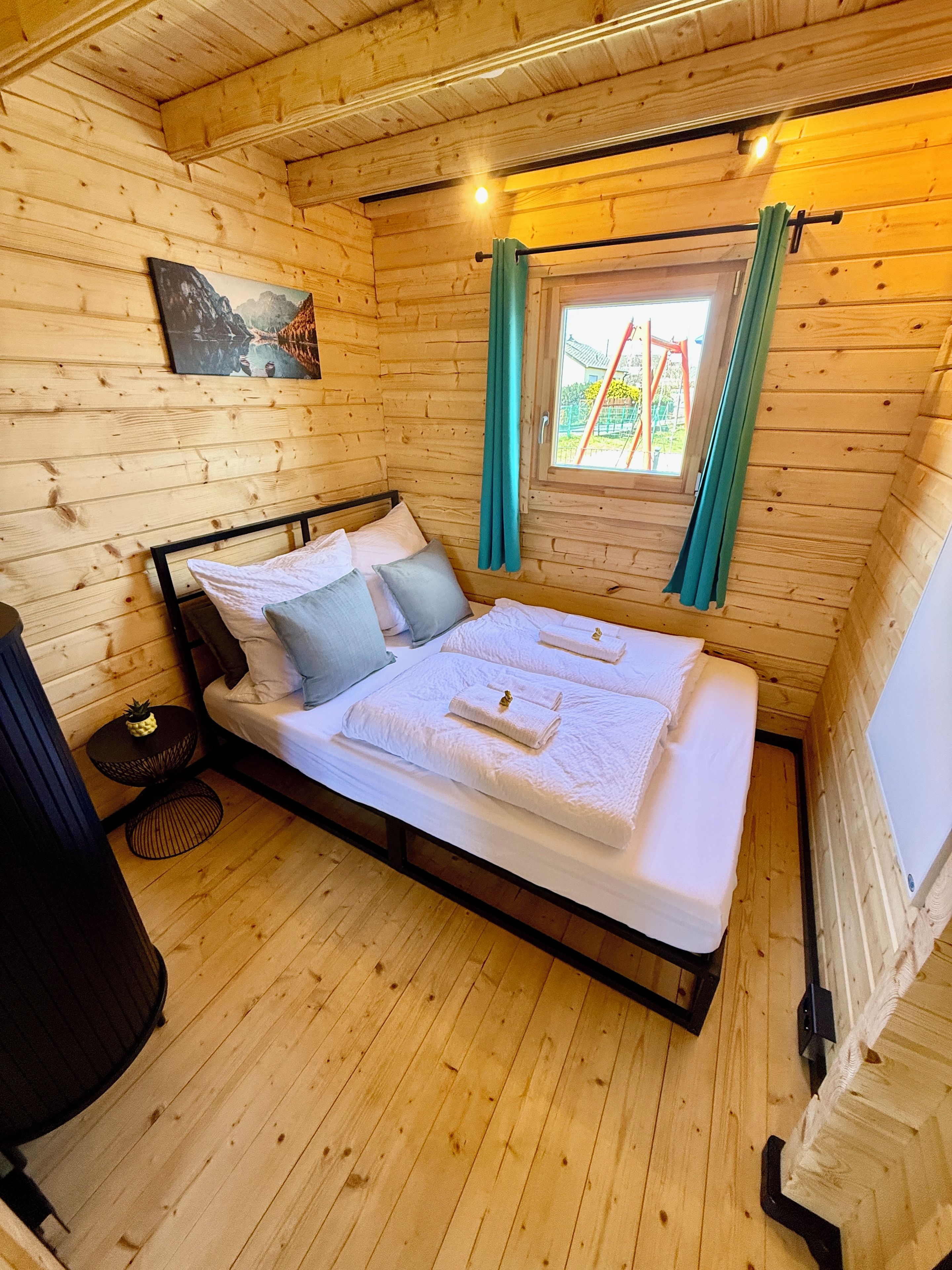 Ein Schlafzimmer einer Holzhütte mit einem Bett, Kissen, einem kleinen runden Tisch und einem Fenster mit Vorhängen.
