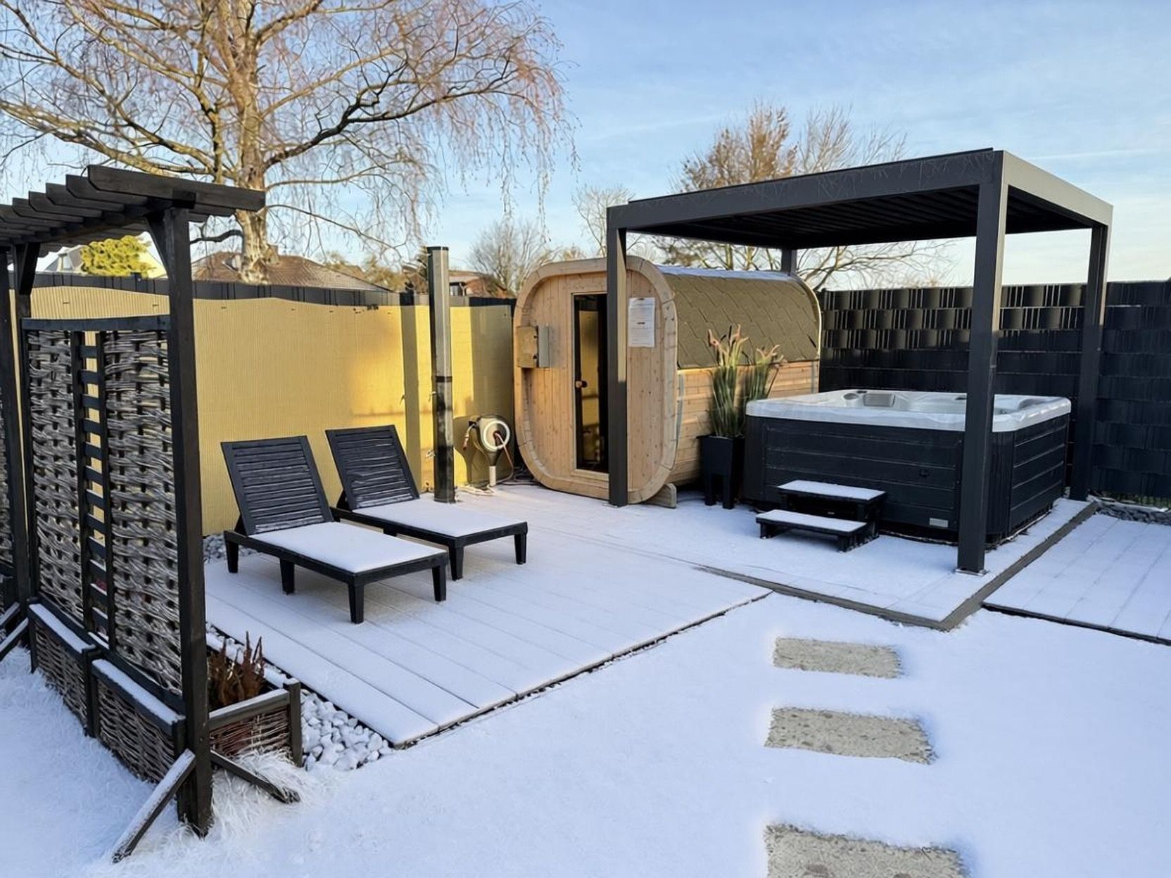 Un espace extérieur enneigé comprenant un jacuzzi, des chaises longues et une structure en bois.