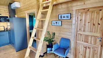 Een houten interieur met een houten ladder, een blauwe stoel, een koelkast en een deur.