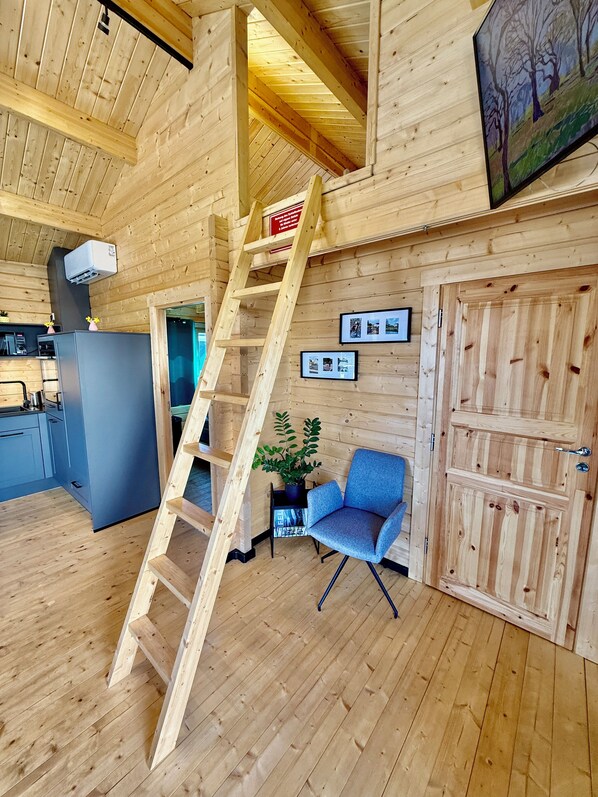 A wooden interior with a wooden ladder, a blue chair, a refrigerator, and a door.
