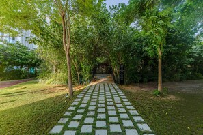 A paved pathway leading through a garden with trees and a building in the background. - HAVN - Prime Studio in Torino Arjan in Garden View (Dubai)