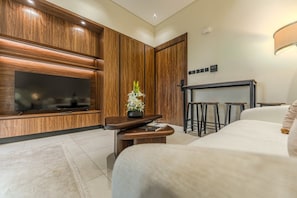 A modern hotel room with a flat-screen TV, wooden paneling, a small table with a vase, and a bed. - HAVN - Prime Studio in Torino Arjan in Garden View (Dubai)