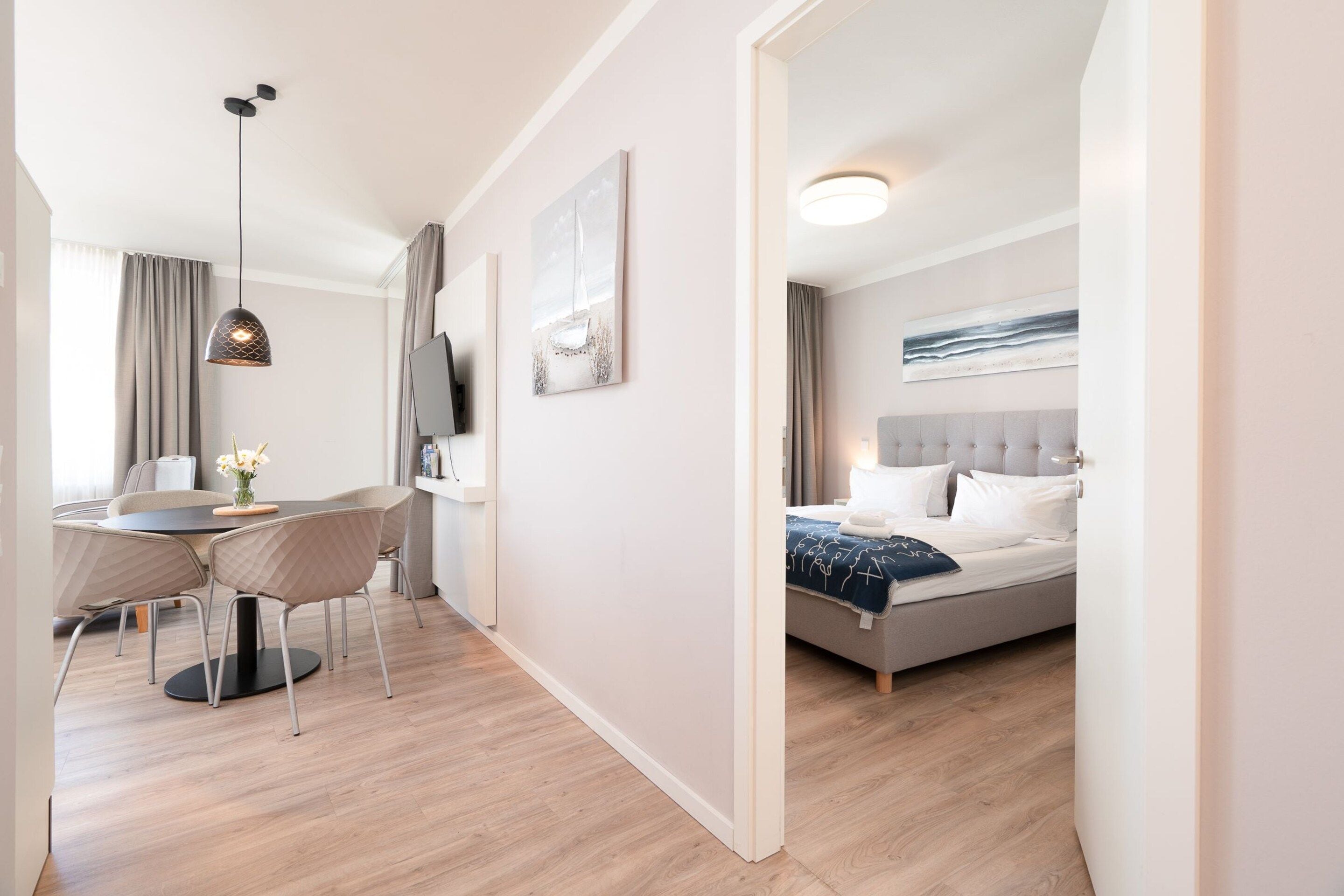 Una habitación de hotel moderna con una cama, un escritorio con sillas, un televisor y obras de arte en las paredes.